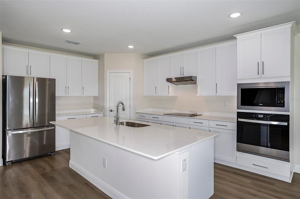 A modern kitchen features white cabinetry, stainless steel appliances, a quartz island, and wood flooring — 31681 BIENVILLE LANE, WESLEY CHAPEL, FL