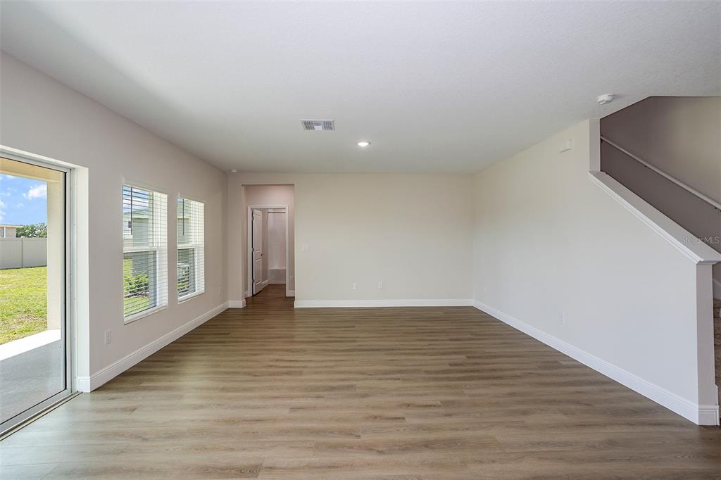 An empty living room features light wood-look flooring, white walls, and a staircase — 31681 BIENVILLE LANE, WESLEY CHAPEL, FL