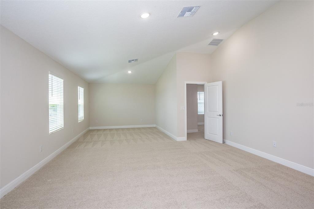 An empty room with beige carpet, light-colored walls, vaulted ceilings, and a white door — 31681 BIENVILLE LANE, WESLEY CHAPEL, FL