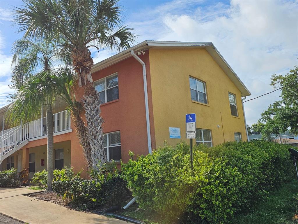 A two-story apartment building with yellow and orange stucco walls and a palm tree — 117 N EVERGREEN AVENUE UNIT 205, CLEARWATER, FL
