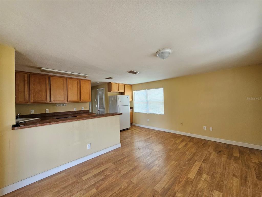 An open-concept kitchen with wood cabinets and a breakfast bar overlooks a living area — 117 N EVERGREEN AVENUE UNIT 205, CLEARWATER, FL