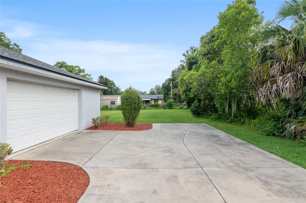 A concrete driveway leads to a garage next to a grassy backyard with trees — 3424 NE 14TH STREET, OCALA, FL