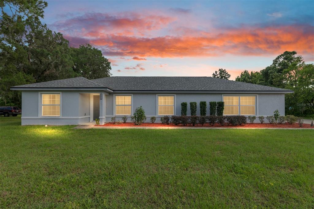 A single-story gray house with a dark roof and red mulch landscaping at sunset — 3424 NE 14TH STREET, OCALA, FL