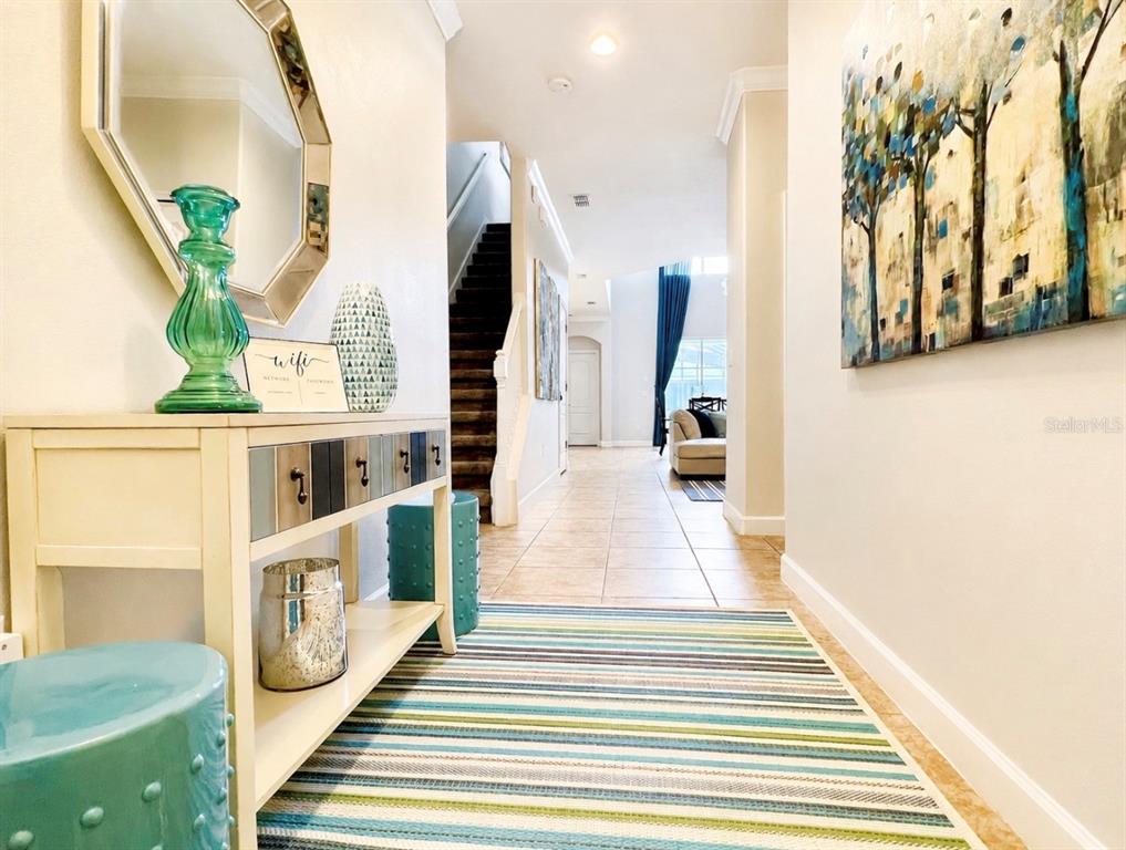A bright entryway features a console table, a striped rug, and stairs leading upward — 8932 BISMARCK PALM ROAD, KISSIMMEE, FL