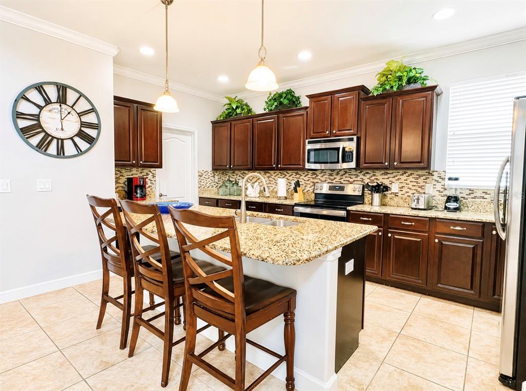 A kitchen features dark wood cabinets, granite countertops, a center island, and tile flooring — 8932 BISMARCK PALM ROAD, KISSIMMEE, FL