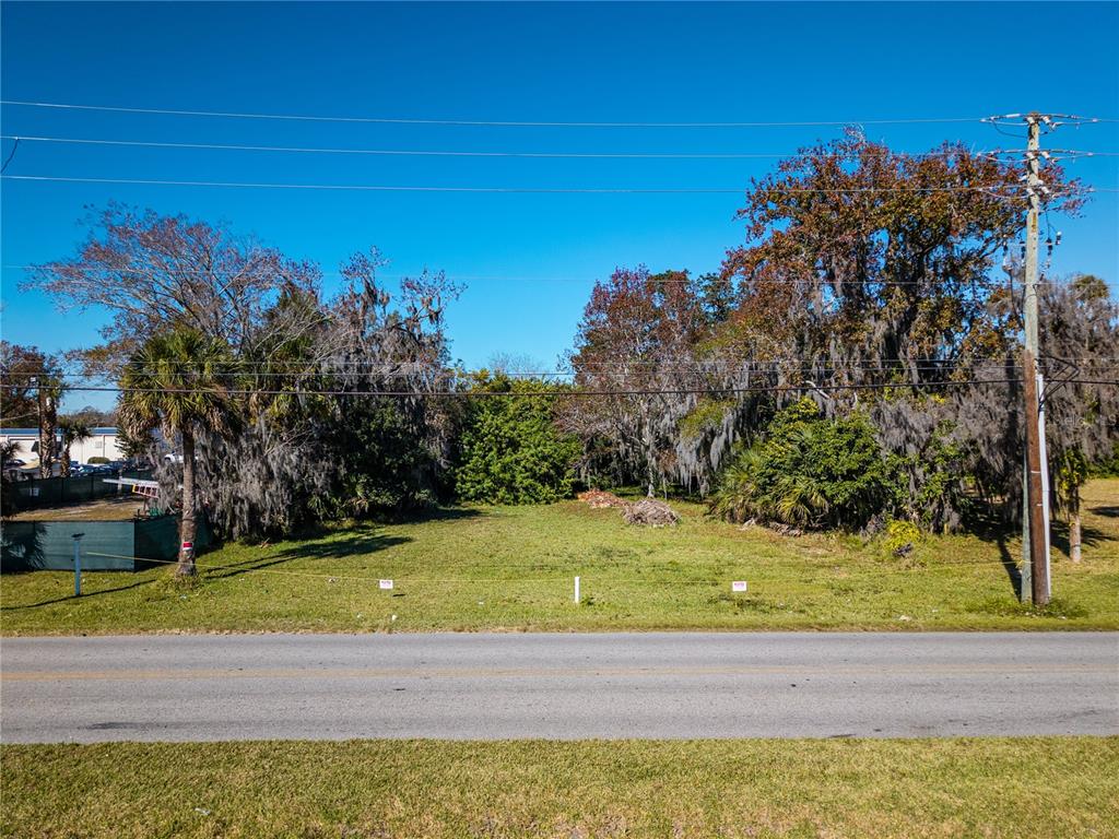 A vacant, grassy lot with trees and utility poles sits alongside a paved road — 818 6TH STREET, DAYTONA BEACH, FL