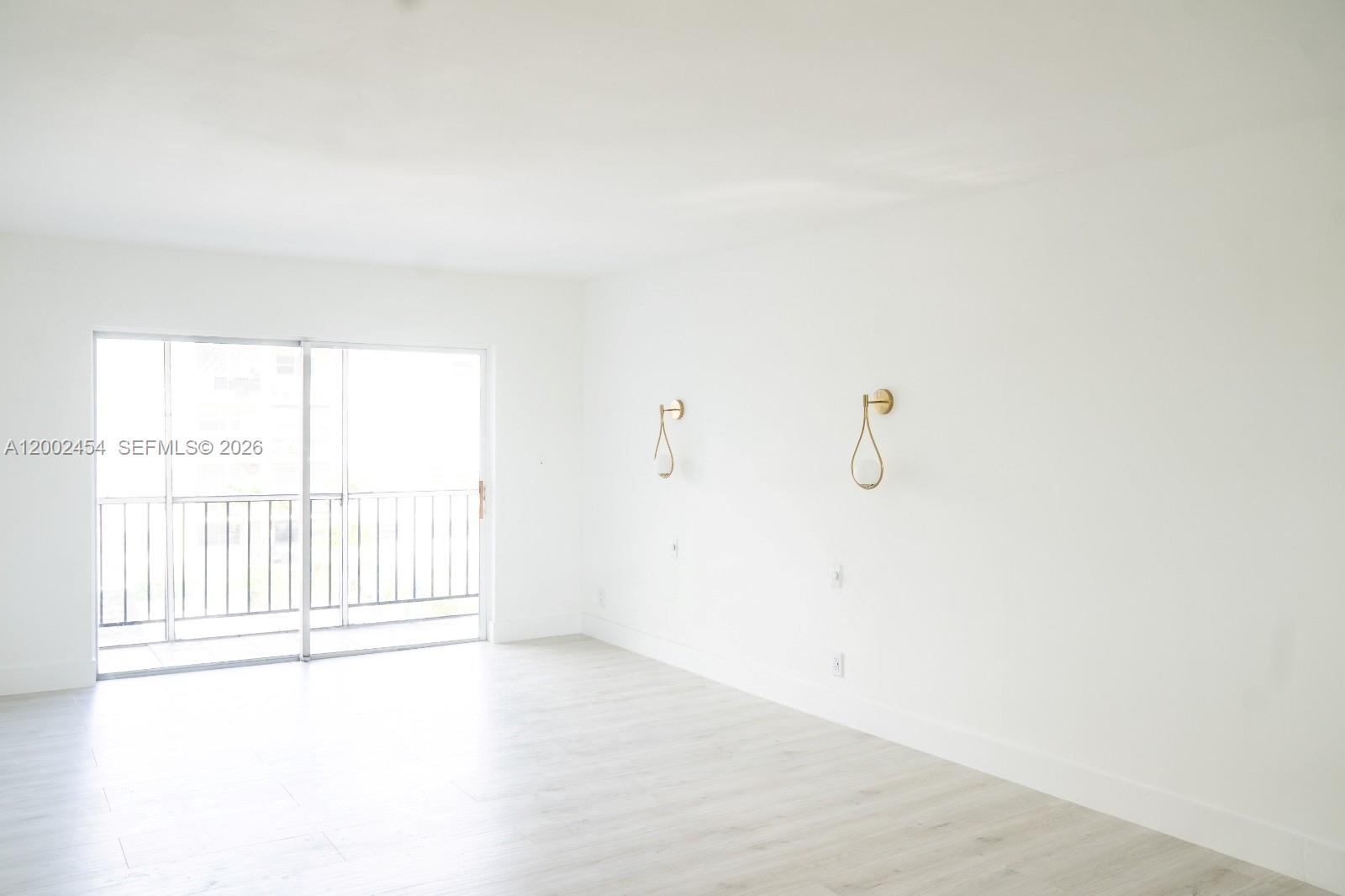 A bright, empty room features white walls, light wood-look flooring, and two gold wall sconces — 220 SW 9th Ave # 306, Hallandale Beach FL 33009, HALLANDALE BEACH, FL