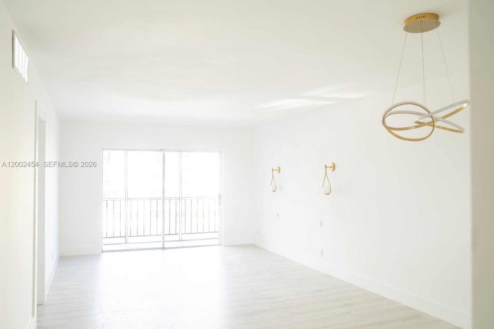 A bright, empty living room features white walls, light wood-look flooring, and a modern chandelier — 220 SW 9th Ave # 306, Hallandale Beach FL 33009, HALLANDALE BEACH, FL