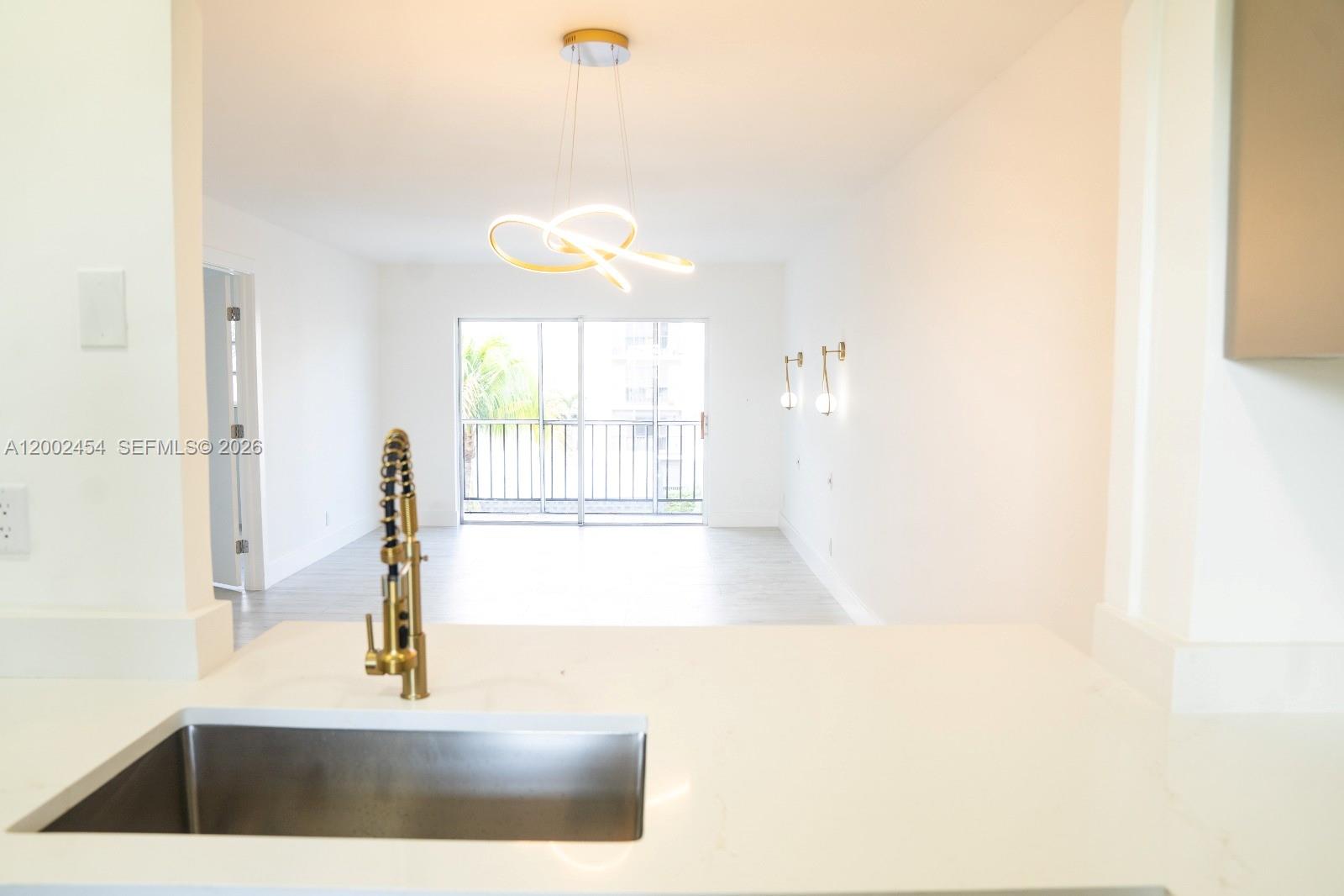 A kitchen sink and faucet overlook an open living area with a modern light fixture — 220 SW 9th Ave # 306, Hallandale Beach FL 33009, HALLANDALE BEACH, FL