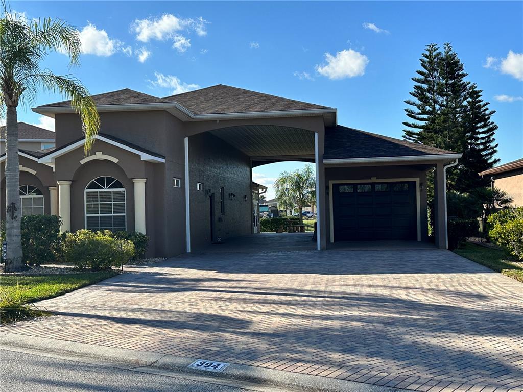 A brown house features a large covered porte-cochère, a dark garage door, and paver driveway — 394 NOLANE LANE, POLK CITY, FL
