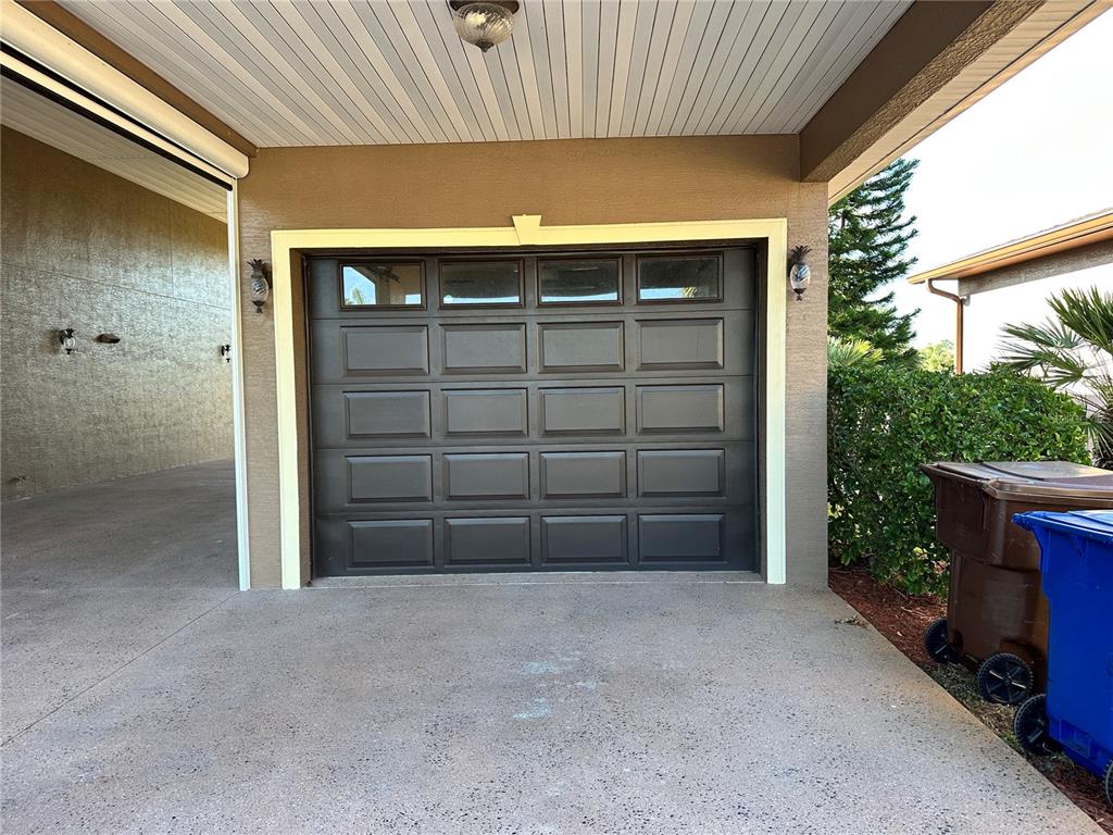 A dark-colored garage door with windows is set within a covered concrete driveway area — 394 NOLANE LANE, POLK CITY, FL