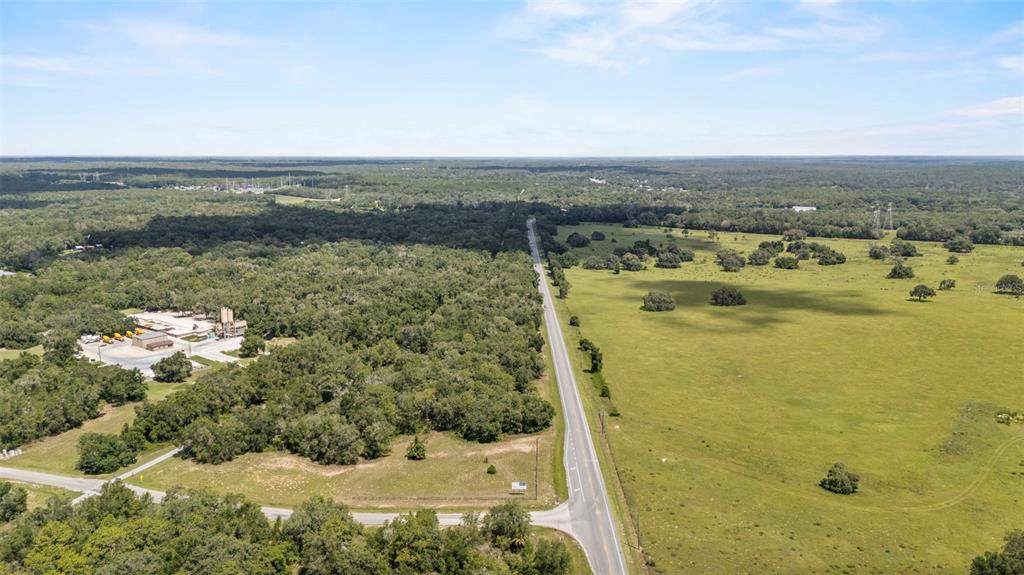 An aerial view shows a road separating a wooded area with buildings from open pasture — 6350 N FLORIDA AVENUE, HERNANDO, FL