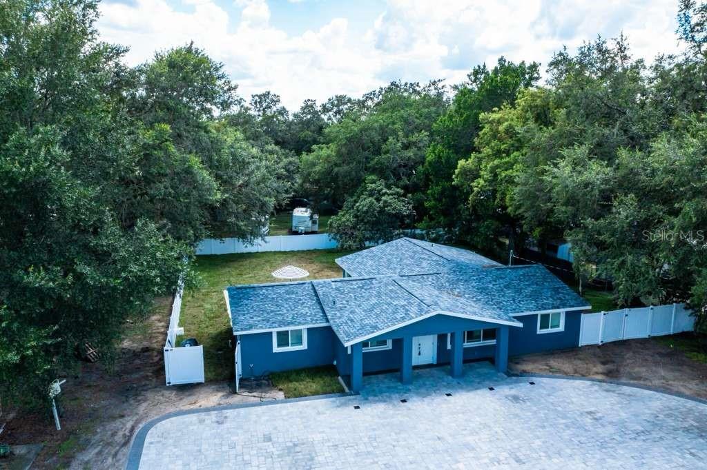 An aerial view shows a blue house with a shingled roof and a paved driveway — 39352 COUNTY ROAD 54, ZEPHYRHILLS, FL