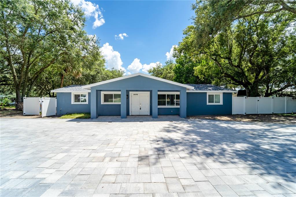 A blue single-story house with a large paved driveway and white vinyl fencing — 39352 COUNTY ROAD 54, ZEPHYRHILLS, FL