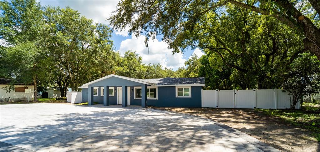 A blue single-story house with a large paved driveway and a white vinyl fence — 39352 COUNTY ROAD 54, ZEPHYRHILLS, FL