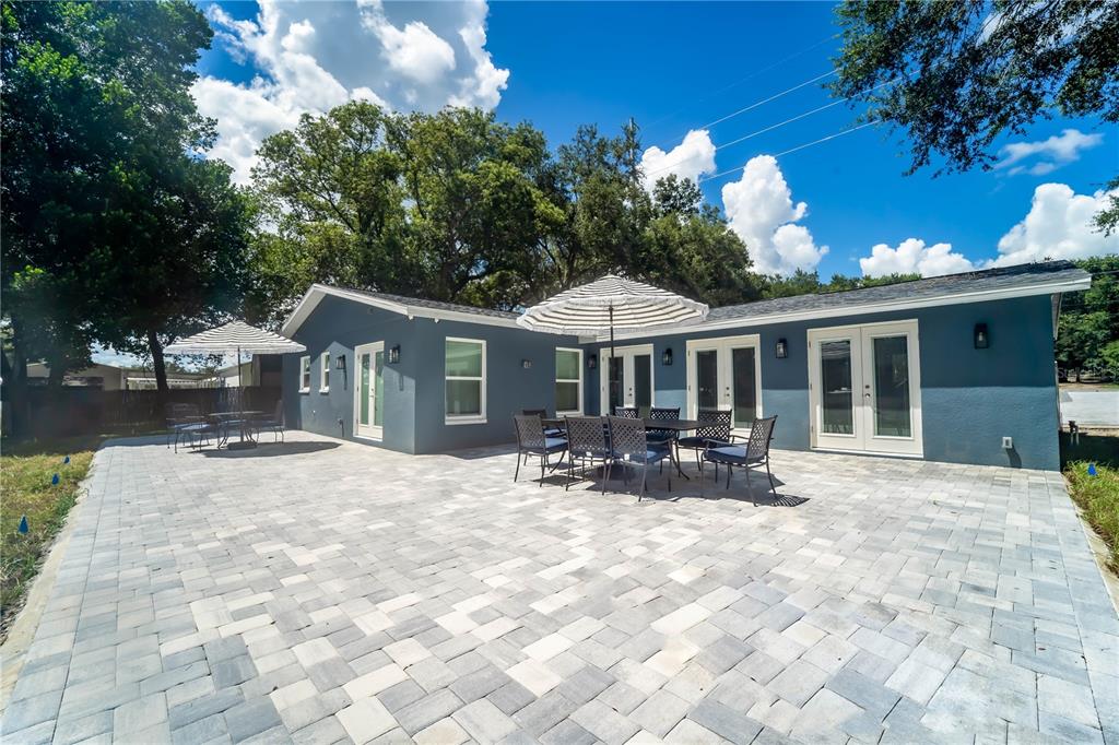 A blue house exterior features a large paver patio with outdoor dining sets and umbrellas — 39352 COUNTY ROAD 54, ZEPHYRHILLS, FL