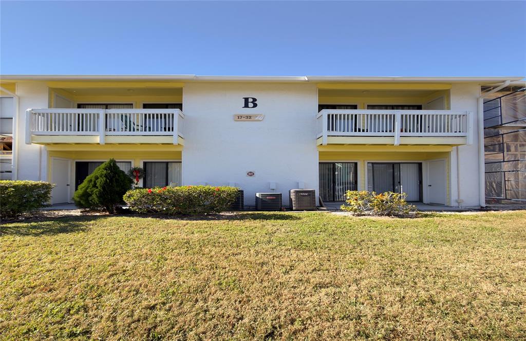 A two-story apartment building exterior features white walls, yellow accents, and balconies on each level — 455 ALT 19 S UNIT 21, PALM HARBOR, FL