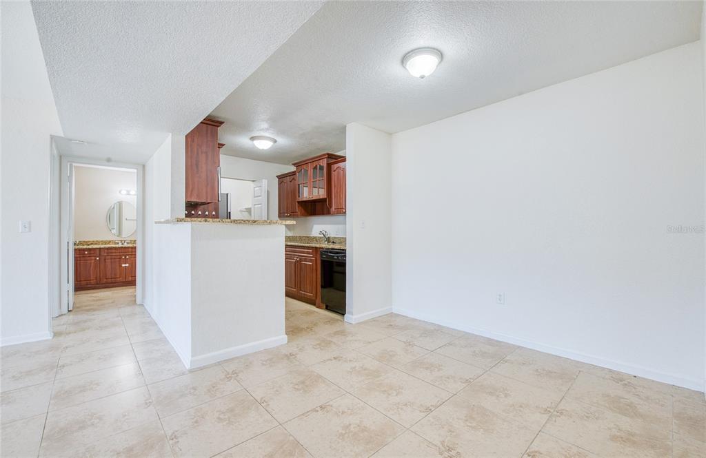 A kitchen with wood cabinets and granite countertops overlooks a tiled dining area — 455 ALT 19 S UNIT 21, PALM HARBOR, FL