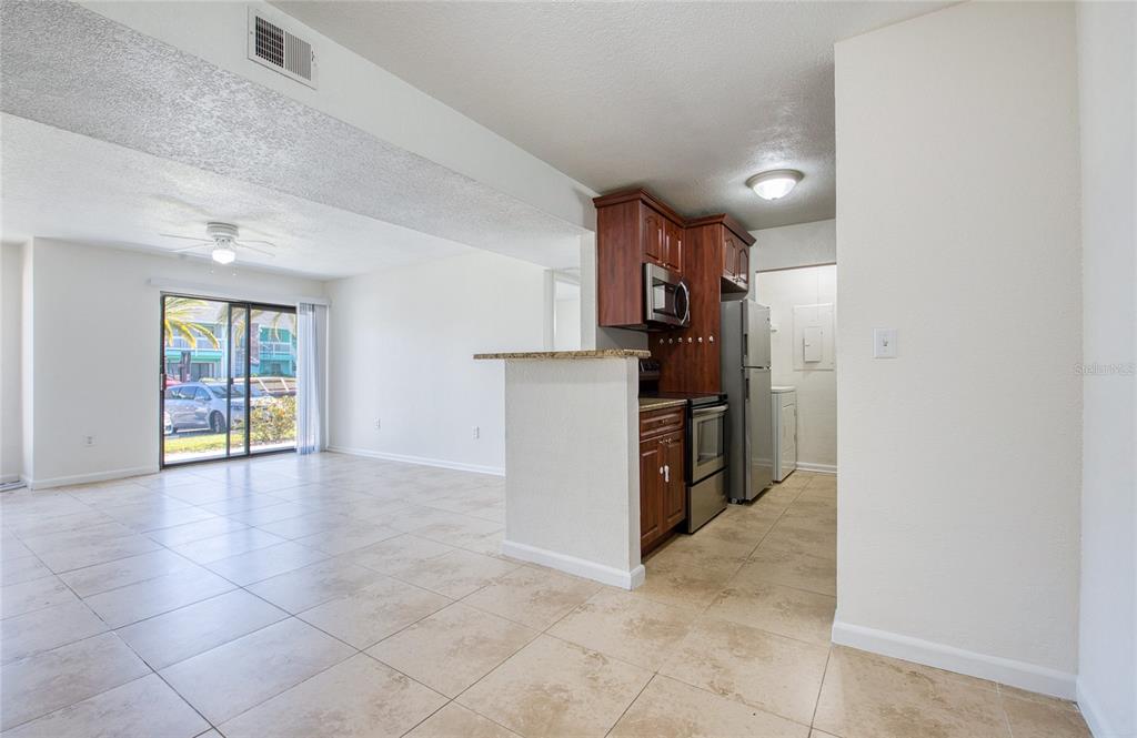 A kitchen with wood cabinets and tile floors opens into a living area with sliding doors — 455 ALT 19 S UNIT 21, PALM HARBOR, FL
