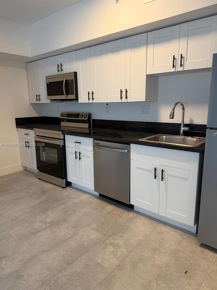A kitchen features white shaker cabinets, black countertops, stainless steel appliances, and gray tile flooring — 147 Nw 59th St # 206, Miami FL 33127, MIAMI, FL