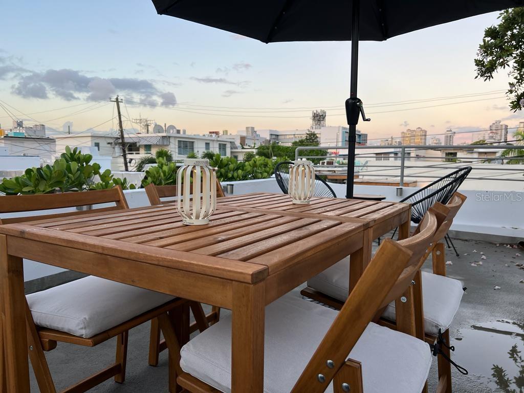 A wooden patio table with chairs and lanterns sits on a rooftop terrace at sunset — 50 Ismael Rivera Street OCEAN PARK UNIT 02, SAN JUAN, PR