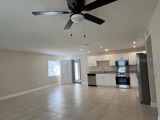 An open-concept kitchen with white cabinetry and stainless steel appliances overlooks a tiled living area — 9004 TUDOR DRIVE UNIT K104, TAMPA, FL