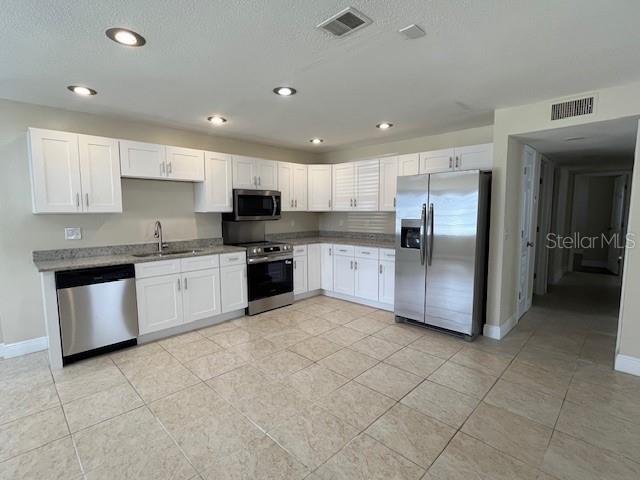 A kitchen features white cabinets, stainless steel appliances, and light-colored tile flooring — 9004 TUDOR DRIVE UNIT K104, TAMPA, FL