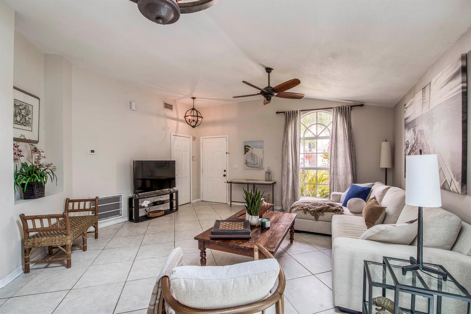 A living room features tile flooring, a beige sectional sofa, a wooden coffee table, and an arched window — 149 Cypress Cove, Jupiter FL 33458, JUPITER, FL