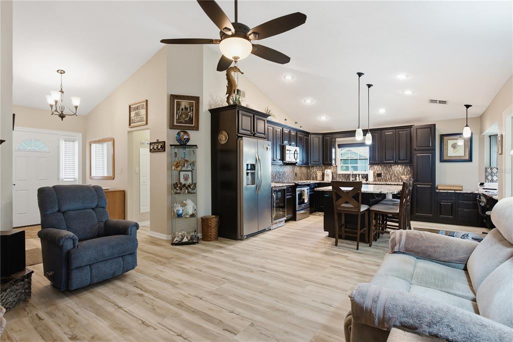 An open-concept kitchen and living area features dark wood cabinets, stainless appliances, and light flooring — 11722 CURRIE LANE UNIT F1, LARGO, FL