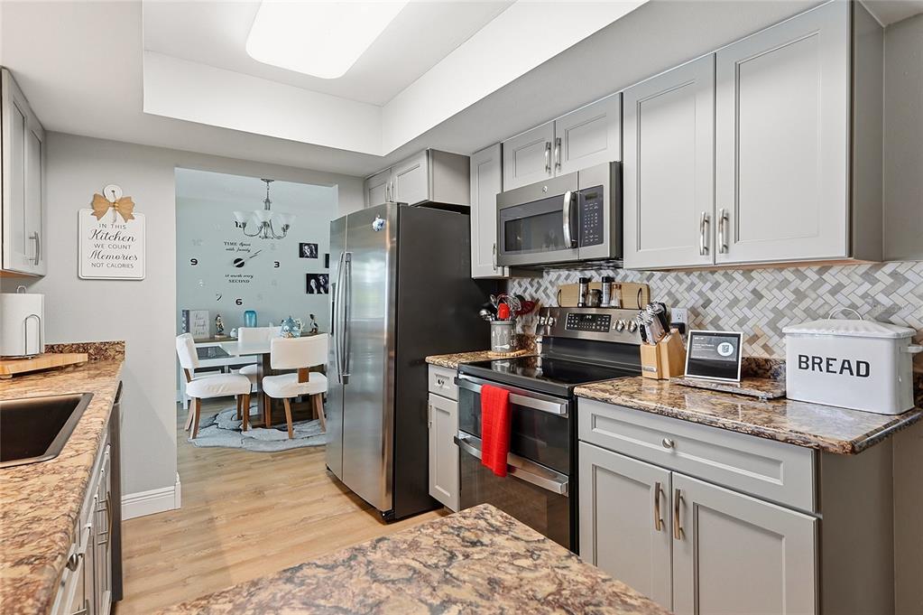 A kitchen with gray cabinets, stainless steel appliances, and granite countertops opens to a dining area — 7219 REYMOOR DRIVE, NORTH FORT MYERS, FL