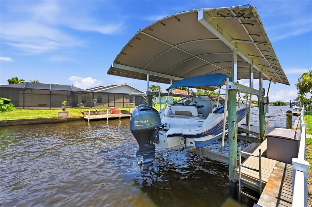 A boat on a lift sits under a canopy next to a canal-side house — 7219 REYMOOR DRIVE, NORTH FORT MYERS, FL