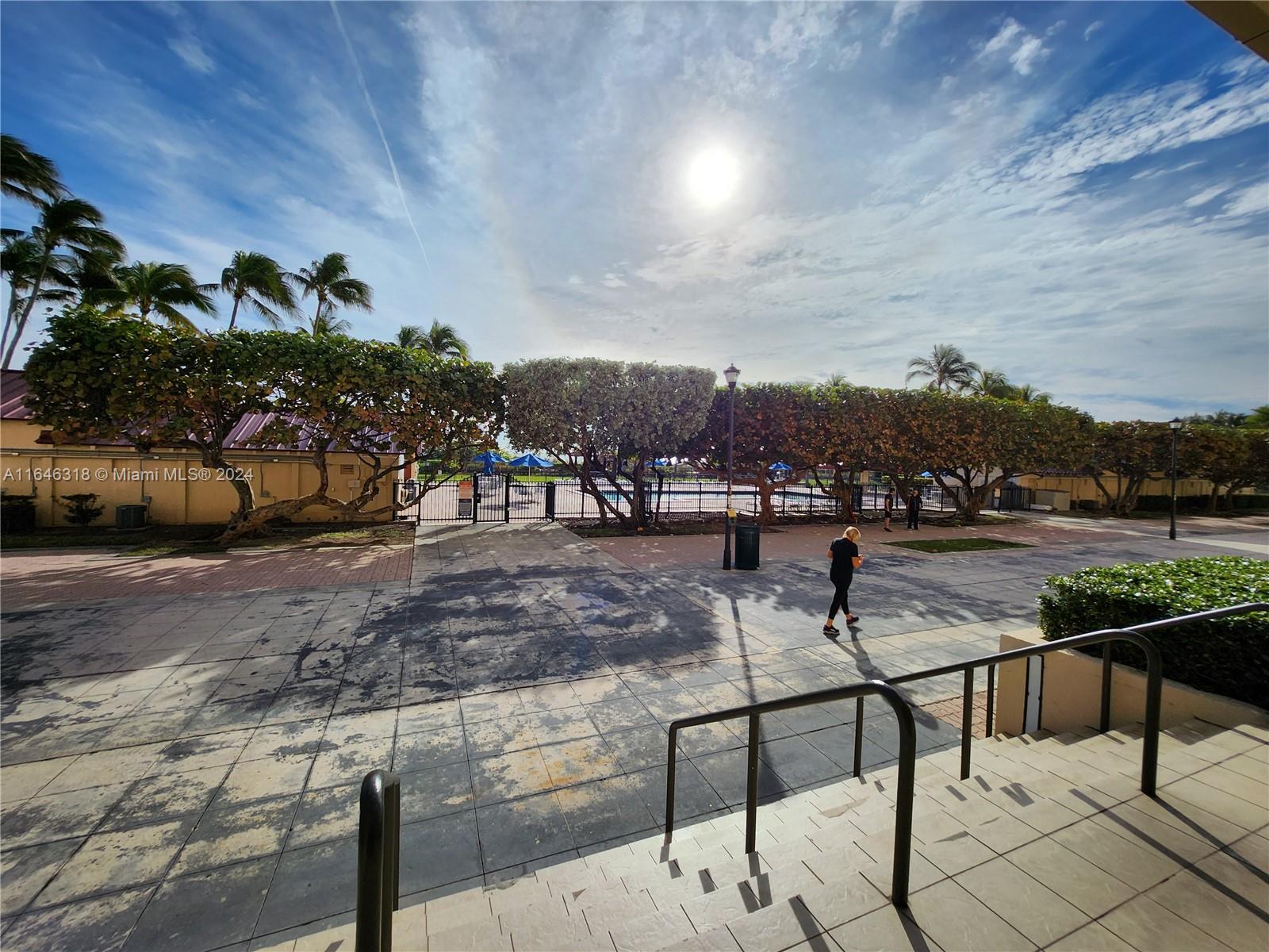 An outdoor walkway leads toward a fenced pool area with palm trees under a sunny sky — 2555 Collins Ave # 306, Miami Beach FL 33140, MIAMI BEACH, FL