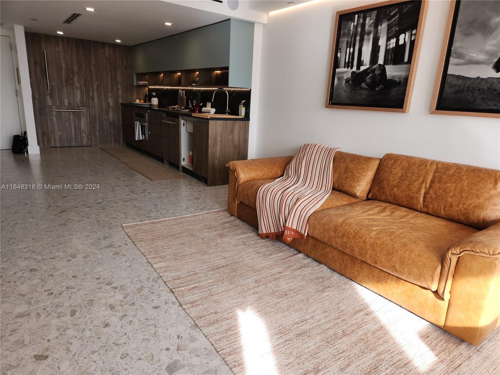 A modern living room features a leather sofa, a patterned rug, and an adjacent kitchen — 2555 Collins Ave # 306, Miami Beach FL 33140, MIAMI BEACH, FL