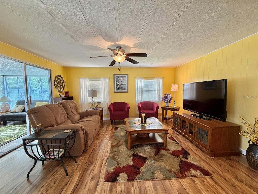 A living room features yellow walls, wood-look flooring, a brown sofa, and two red chairs — 126 CHESTNUT STREET, LEESBURG, FL