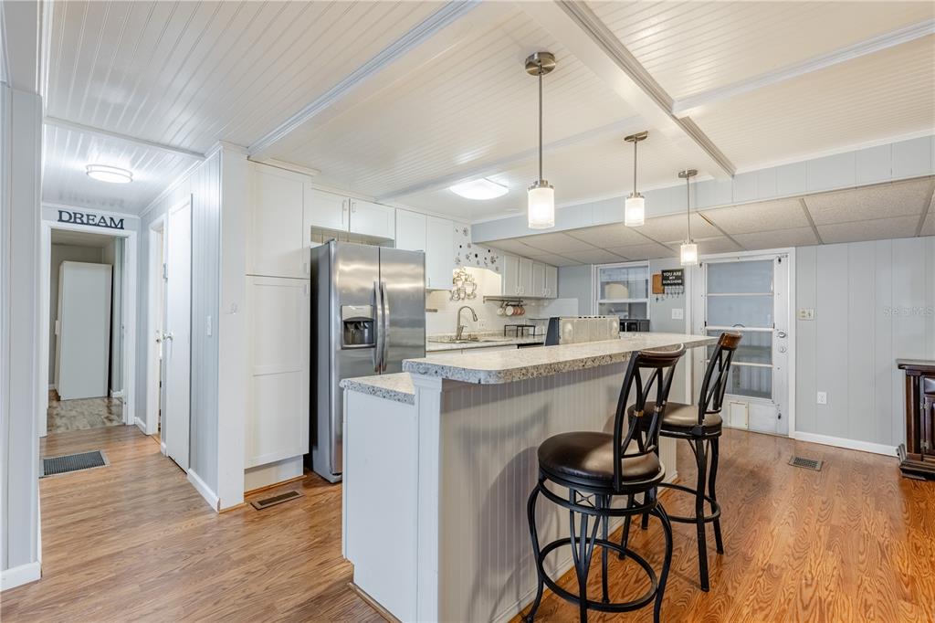 A kitchen features white cabinetry, a granite-topped breakfast bar with two stools, and wood flooring — 1030 CAPELLA DRIVE, TAVARES, FL