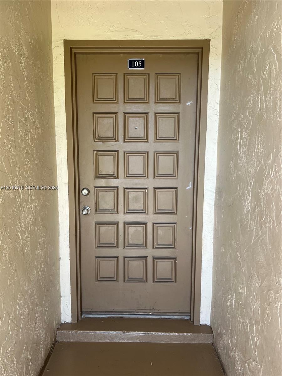 A brown front door with a number 105 plaque is set within a textured alcove — 7775 SW 86th St # 105, Miami FL 33143, MIAMI, FL