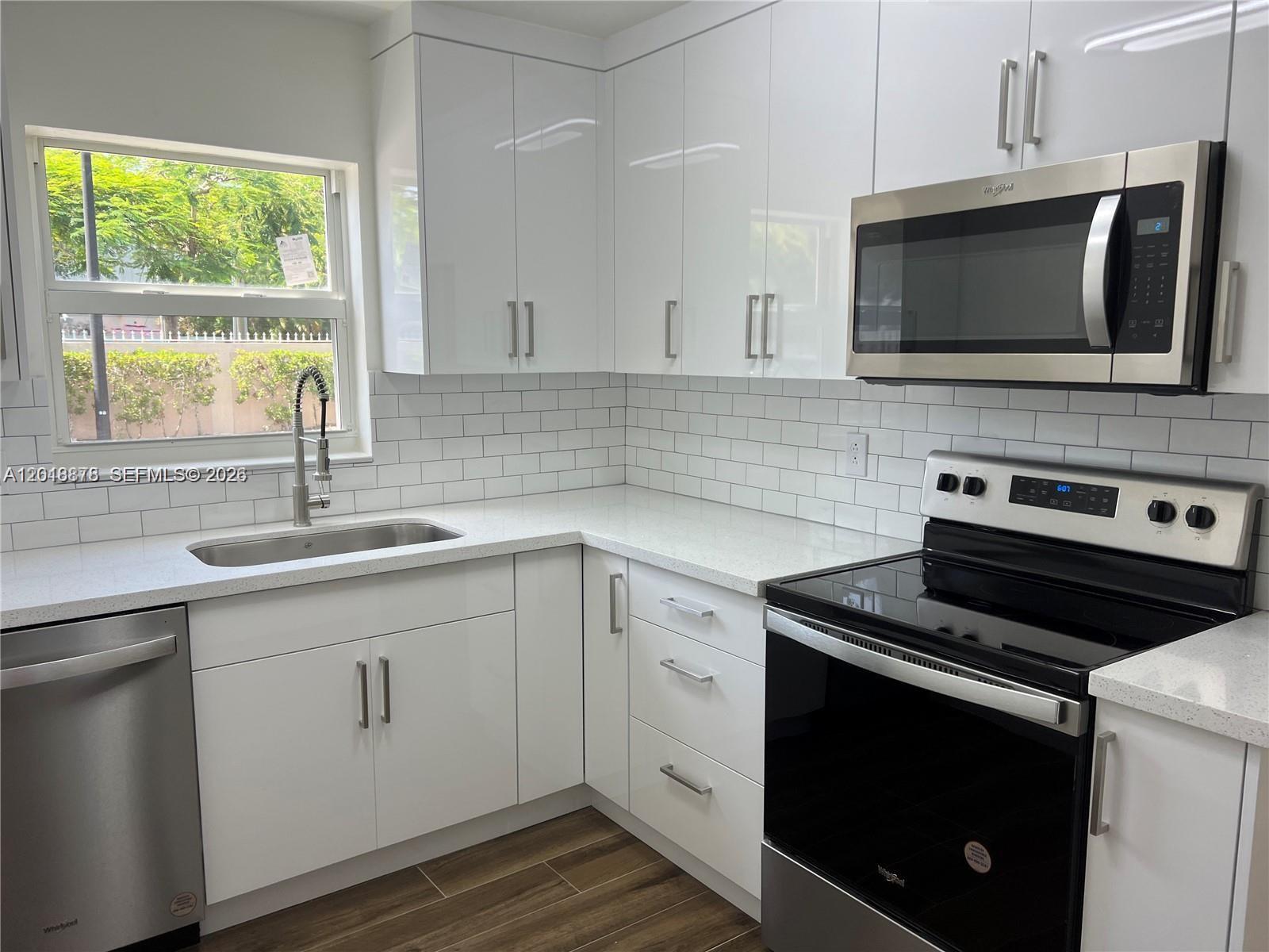 A modern kitchen features white glossy cabinets, stainless steel appliances, and a white subway tile backsplash — 7775 SW 86th St # 105, Miami FL 33143, MIAMI, FL