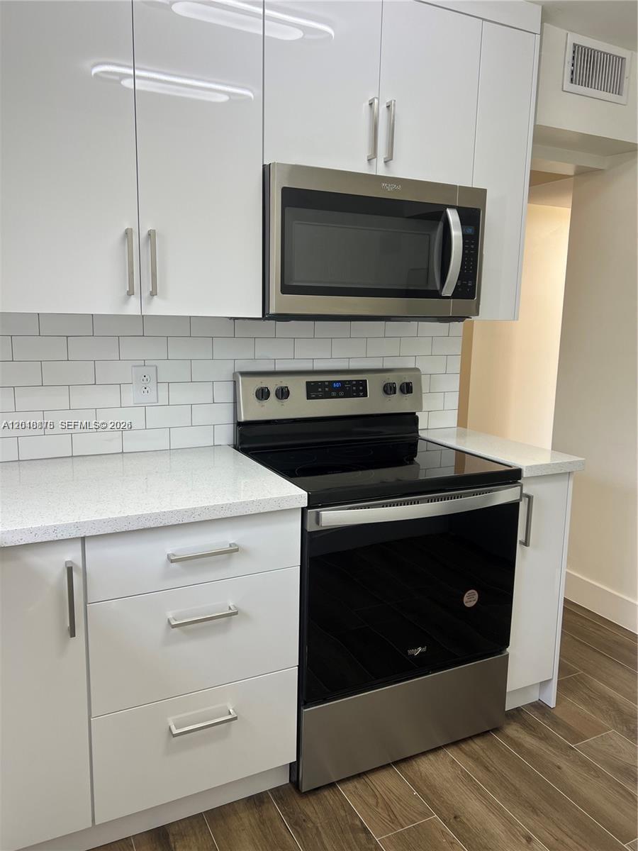A modern kitchen features white cabinets, stainless steel appliances, a subway tile backsplash, and countertops — 7775 SW 86th St # 105, Miami FL 33143, MIAMI, FL
