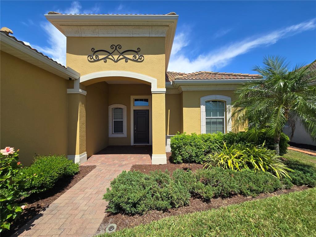 The exterior of a yellow stucco house features a covered entryway with a decorative metal accent — 1358 STILL RIVER DRIVE, VENICE, FL