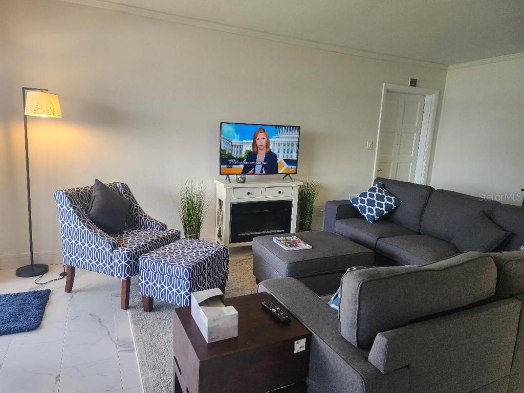 A living room features a gray sectional sofa, a patterned armchair with ottoman, and a television — 1003 S BAYSHORE BOULEVARD UNIT 202, SAFETY HARBOR, FL
