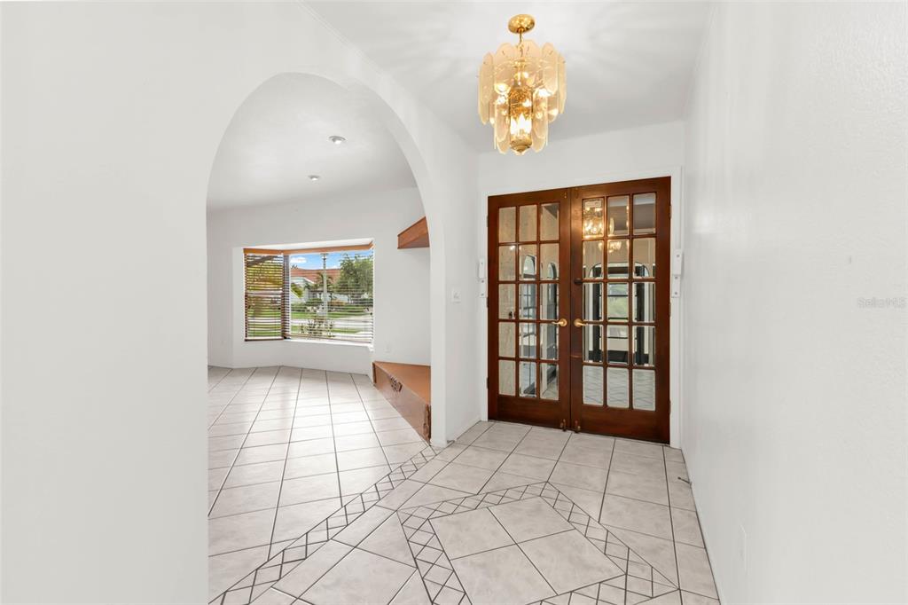 An entryway with white tile floors, a gold chandelier, and double glass-paned wooden doors — 238 FRY TERRACE SE, PORT CHARLOTTE, FL