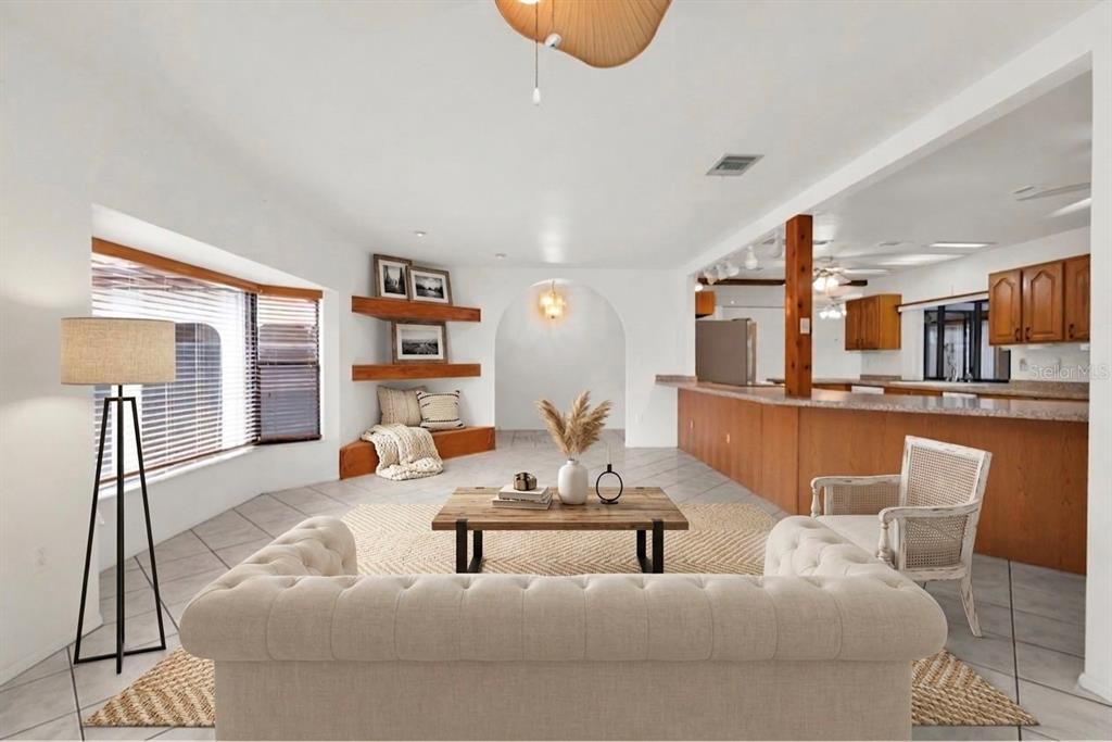 A living room with a tufted sofa, wooden coffee table, corner shelving, and an open kitchen — 238 FRY TERRACE SE, PORT CHARLOTTE, FL