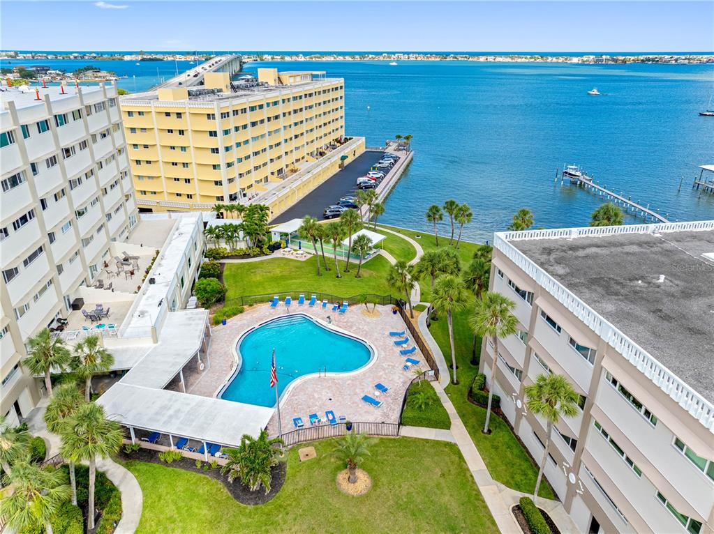 An aerial view shows a swimming pool between two apartment buildings near a bay — 100 BLUFF VIEW DRIVE UNIT 404C, BELLEAIR BLUFFS, FL