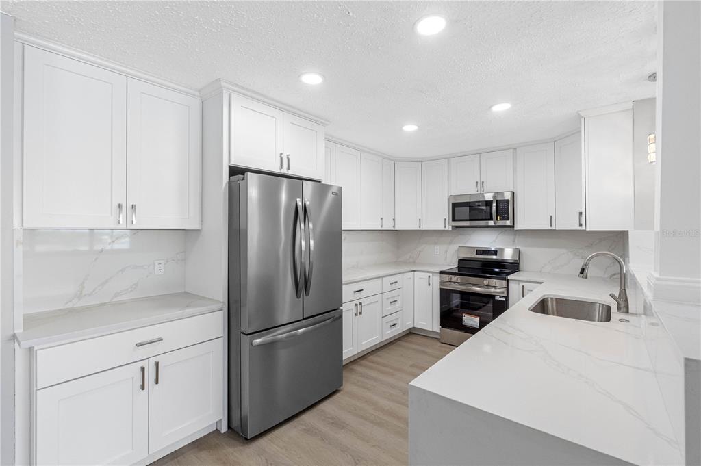 A modern kitchen features white cabinets, stainless steel appliances, and white marble-patterned countertops — 100 BLUFF VIEW DRIVE UNIT 404C, BELLEAIR BLUFFS, FL