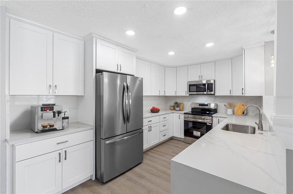 A modern kitchen features white cabinets, stainless steel appliances, and white quartz countertops — 100 BLUFF VIEW DRIVE UNIT 404C, BELLEAIR BLUFFS, FL