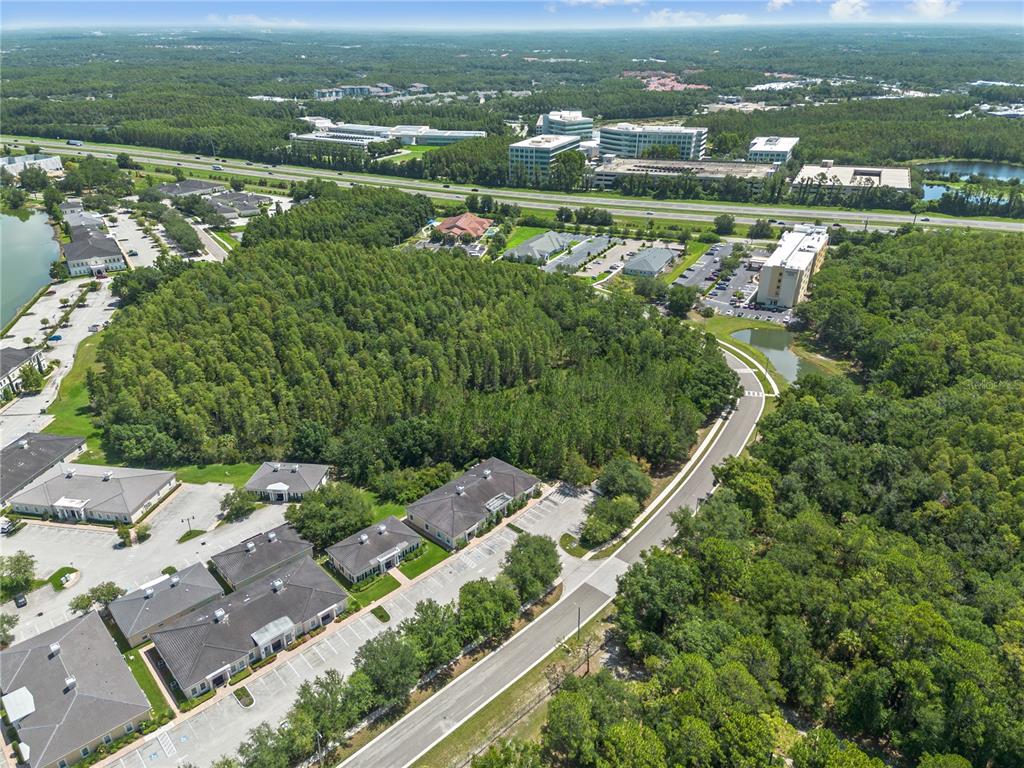 An aerial view shows a wooded lot surrounded by commercial buildings, parking lots, and roads — 5381 PRIMROSE LAKE CIRCLE, TAMPA, FL