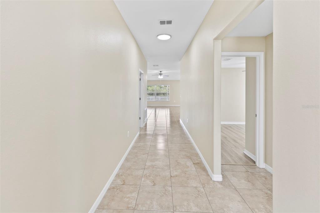 A long hallway with beige tile flooring leads toward a windowed living area — 10633 STANDING STONE DRIVE, WIMAUMA, FL