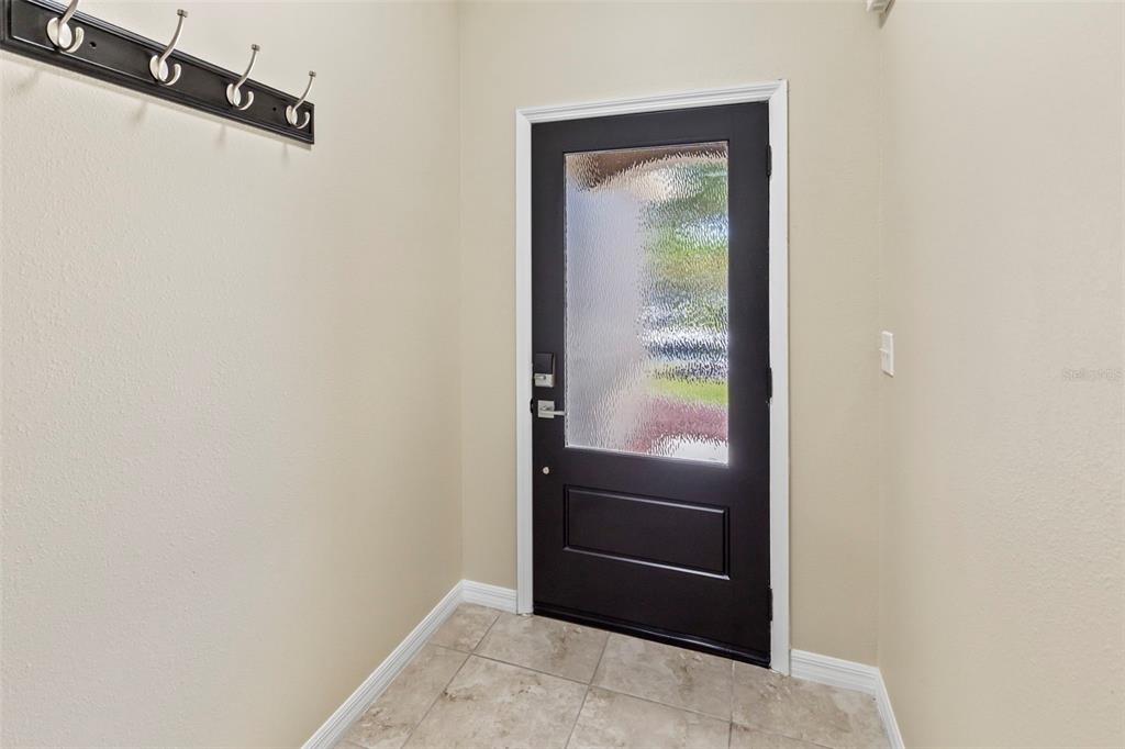 An entryway features a black front door with textured glass, tile flooring, and a wall-mounted rack — 10633 STANDING STONE DRIVE, WIMAUMA, FL