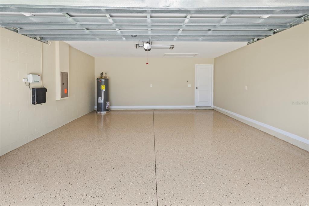 A clean, empty garage features a speckled epoxy floor, a water heater, and a white door — 10633 STANDING STONE DRIVE, WIMAUMA, FL