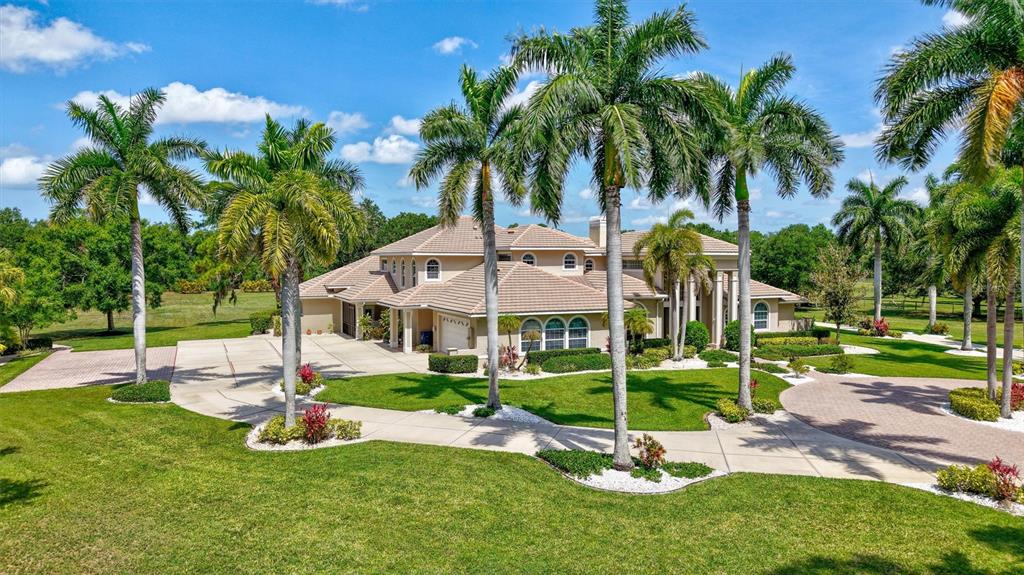 A large tan house with a tiled roof features a spacious concrete driveway and palm trees — 1045 FOX CREEK DRIVE, SARASOTA, FL